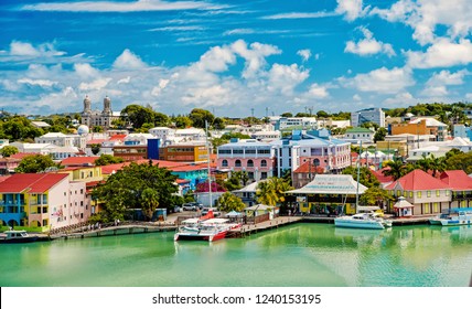 St. John, Antigua - March 05, 2016: Cute Houses At Harbor With Yacht, Boat, Ship Transportation In Bay With Sea, Ocean Water, Blue Cloudy Sky Sunny Summer On Natural Background. Traveling And Vacation