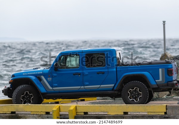 St. John\'s, Newfoundland, Canada, April 2022: A vibrant\
blue Jeep Gladiator Rubicon truck 4x4 off road and parked on the\
side of a hill with the blue ocean, blue sky, and clouds in the\
background. 