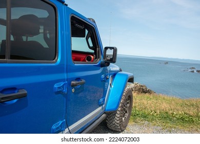 St. John's, Newfoundland, Canada, November 2022: A Vibrant Blue Jeep Gladiator Rubicon Truck 4x4 Off Road And Parked On A Rocky Hill And Path With Yellow Grass And Blue Ocean In The Background. 