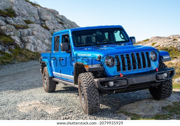St. John\'s, Newfoundland, Canada, November 2021: A\
vibrant blue Jeep Gladiator Rubicon truck 4x4 off road and parked\
on the side of a hill with the blue ocean, blue sky, and clouds in\
the background. 