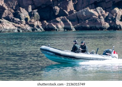 St. John's, Newfoundland, Canada-March 2022: Two armed military sailors patrolling a Canadian coastline in a zodiac motorized boat. The armed tactical soldiers are in a rubber boat surveilling. 