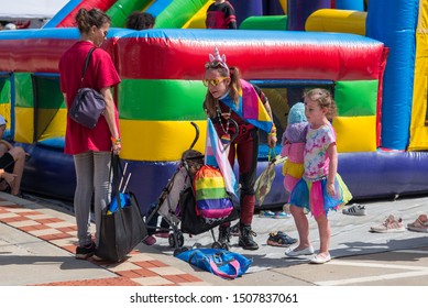 St. Joseph, Missouri / United States Of America -September 14th 2019 : People In Costume Near A Rainbow Bounce House, With A Stroller And Small Children.  During Pridefest.