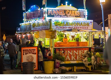 St. Joseph, Missouri / United States Of America - October 11th, 2019: Carnival Funnel Cake Stand Lit Up At Night.  Fresh Squeezed Lemonade, Jumbo Hot Pretzels.  People In Line Waiting.