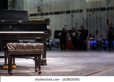 St. Joseph, MO / United States Of America - Oct 14th 2019: A Steinway And Sons Grand Piano And Bench Sit On Stage, While A Cast And Crew Prepare For A Dress Rehearsal In The Background Of The Theater.