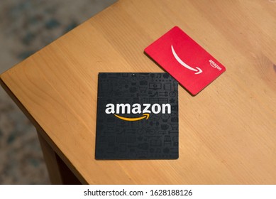 St. Joseph, MO / United States of America - January 24th, 2020 : Two Amazon gift cards on a wooden table. Large black Amazon gift card package, and smaller credit card sized red single gift card.
