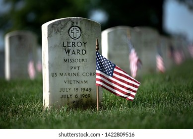 St. Louis, MO, USA, May 26, 2019 - Closeup Of White Military Headstone At Burial Sites With American Flags In Jefferson Barracks Military Cemetery With Rows Of Headstones In Background