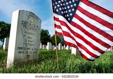 St. Louis, MO, USA, May 26, 2019 - Wide Angle Closeup Of White Military Headstone At Burial Site With American Flags And Rows Of Headstones In Background At Military Cemetery
