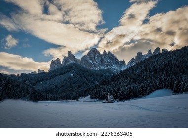 St. Magdalena or Santa Maddalena with its characteristic church in front of the Geisler or Odle dolomites mountain peaks in the Val di Funes Villnosstal in Italy in winter. January 2023. Long exposure