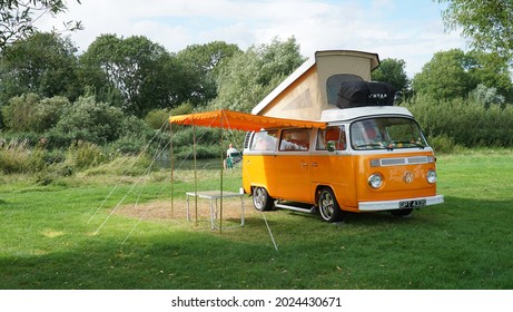 ST NEOTS, CAMBRIDGESHIRE, ENGLAND -  AUGUST 13, 2021: Classic  Orange  Volkswagen  Camper Van parked on Camp Site  by river with top up and Awning .