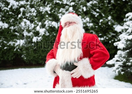St. Nicholas looking at the camera for the New Year and Christmas in a red fur coat, holding his hands on his belt against the background of the forest, Christmas trees, the holiday of Coca-Cola