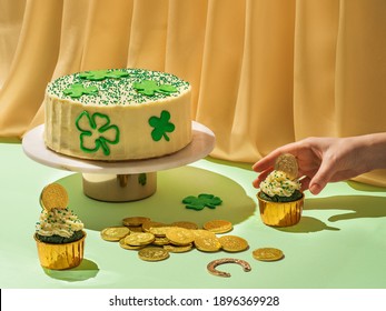 St Patrick's Day food concept. Modern still life with sweet food for Saint Patrick's Day party with female hand. Cake decorated shamrocks, green velvet cupckakes, chocolate golden coins and horseshoe - Powered by Shutterstock