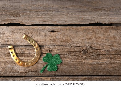 Día de San Patricio. Herradura de oro y hoja de trébol decorativa verde sobre mesa de madera, capa plana. Espacio para texto