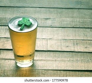 St. Patricks Day Green Shamrock Floating In A Cold, Frosty Glass Of Beer On A Rustic Wood Background With Room Or Space For Copy, Text, Words.  Vintage Camera Instagram Treatment For Mood Effect.  