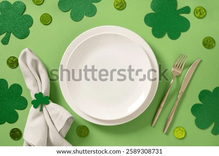 St Patrick's Day table setting with white plate and traditional decoration, shamrock, clover leaves and coins on light green background. View from above.