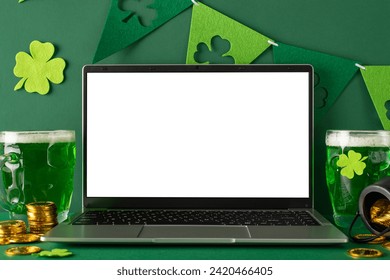 St. Patrick's Day theme: side view photo of laptop open for virtual celebrations, frothy beer mugs, scattered gold coins, pot, and trefoil flag streamers on a vibrant green surface with space for text - Powered by Shutterstock