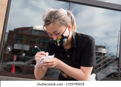 ST PAUL, MINNESOTA / USA - MAY 02, 2020: Server At The Restaurant Writing Name And Order For Curbside Service With Mask In Keeping Social Distance For Coronavirus Covid-19. 