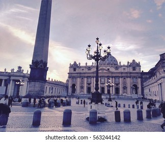 St. Peter Basilica retro photo from square perspective with obelisk, sky with clouds, tourists and vintage lamp post, Vatican Rome