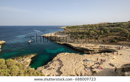 St. Peter's Pool in summer, Marsaxlokk, Malta - natural pool wide angle view, motor boat, tourists enjoying the environment