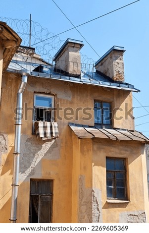 St. Petersburg facade of yellow house of communal apartment with windows in sunny day and roof against background of blue sky. Warm earthy shades Authentic view of old city Dark walls muck up