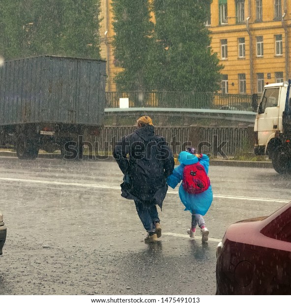 St.\
Petersburg, Russia - August 8 2019: Get caught in the rain. Mother\
and daughter hurry home in the pouring\
rain