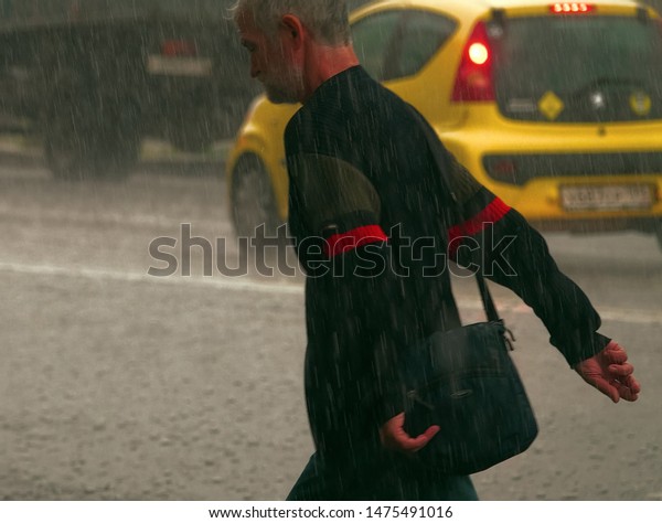 St. Petersburg, Russia - August\
8 2019: Passer-by in the rain on the road among the cars. Pouring\
rain. When it doesn\'t matter if you get wet or not. Rain\
Man