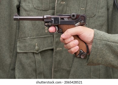St. Petersburg, Russia, July 08, 2021: Historical reenactment of World War II. Luger pistol in hand against the background of the green uniform of a German soldier.