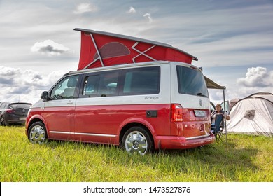 St. Petersburg, Russia - July 22, 2019: Red and white colored modern Volkswagen Multivan California Ocean (Transporter T6). Parked on the camping field. Back side left view