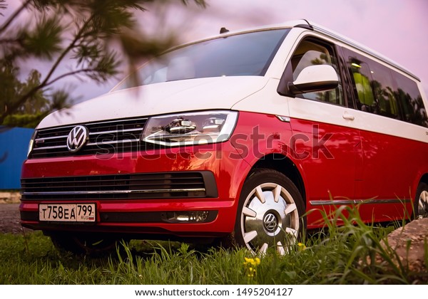 St.\
Petersburg, Russia - July 22, 2019: Red and white colored modern\
Volkswagen Multivan California Ocean (Transporter). Is Parked in\
the forest at sunrise. Hood and led\
headlights