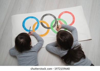 St. Petersburg, Russia, May 25, 2021: Children's Drawing A Symbol Of Sports Olympics. Children Draw Olympic Rings. Children Draw With Colored Pencils. Girl Takes A Pencil From Her Sister.