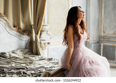 
St. Petersburg, Russia - September 25, 2019: A Beautiful Young Girl In A Lilac Dress, The Bride In An Unusual Way, Her Lips Temporarily Sits Sexually On The Bed. Rock And Roll And Wedding, Originalit