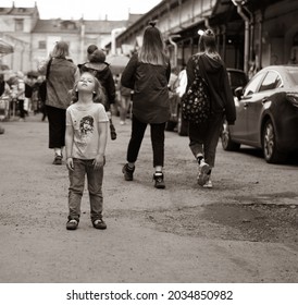 St. Petersburg, Russia-May 15, 2021. A little tired girl is standing with her head thrown back in the middle of the street at people passing by her, a black-and-white picture