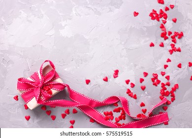 St. Valentine day background.  Gift box with red ribbon  and many little  decorative red hearts on textured concrete.Place for text.