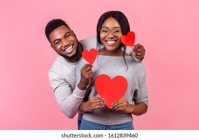 St. Valentines Day Concept. Cheerful Afro Couple In Love Holding Red Valentines Cards And Embracing, Pink Studio Background