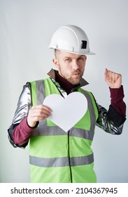 St. Valentine's Day: Dancing Bearded Male Construction Worker Or Technician In Hard Hat And Reflective Vest Holding White Paper Heart Shape. Romance Or Relationships Concept. High Quality Image