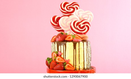 St Valentine's Day on-trend candyland fantasy drip novelty cake decorated with heart shaped lollipops, candy and fresh strawberries.