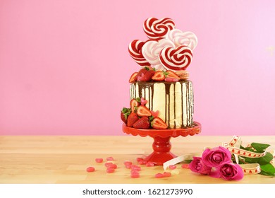 St Valentine's Day on-trend candyland fantasy drip novelty cake decorated with heart shaped lollipops, candy and fresh strawberries, with negative copy space.