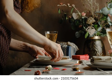 St. Valentines day table setting. Young woman puts plate on served table. Valentines day table decoration. Romantic festive dinner for two persons.