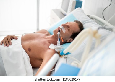 Stable condition. Side view portrait of patient on mechanical ventilator lying in bed under white sheets