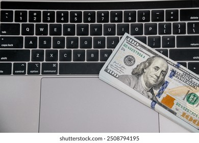 A stack of 100 dollar bills on a laptop keyboard symbolizes financial success, digital transactions and online business. Ideal for promoting e-commerce and modern financial services. - Powered by Shutterstock