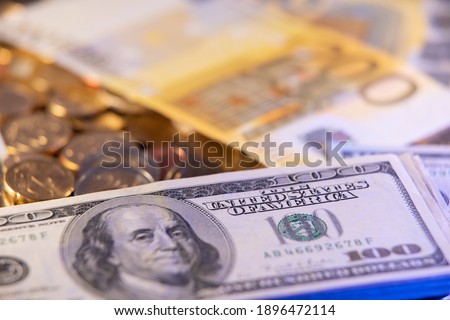 Stack of 100 dollar bills on top of euro coins and European money. United States monetary system