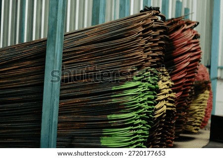 Stack of 16mm rebar featuring painted ends (green and red), indicating specific grades or SNI compliance. The splash of color against the industrial grey steel creates a focal point. This coding system is vital for identifying material properties in a large inventory. The image conveys themes of regulation, standardization, and quality assurance in the construction industry, making it highly relevant for trade publications and safety manuals.