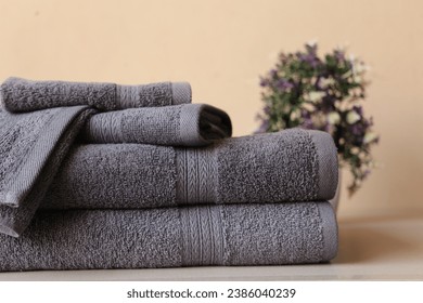 Stack of 2 Arrow Fancy Grey Bath Towels, 1 Hand Towel, and 2 Wash Cloths, Isolated on a Beige Background with a Blurred Backdrop Featuring Lush Plants
