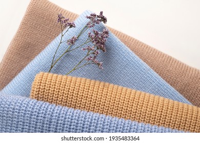 A stack of 4 female wool sweaters of different knitting patterns and colors with a lilac delicate flowers. As a concept for the care of delicate fabrics.