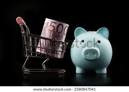 A stack of 500 euro bills and miniature shopping trolley from a supermarket on a black background