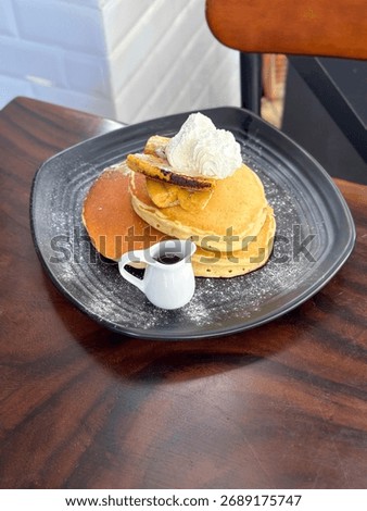 Stack of American style pancakes with maple syrup, banana and squirty cream