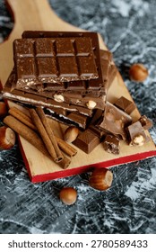 Stack of assorted chocolate bars with hazelnuts and cinnamon sticks on a wooden board