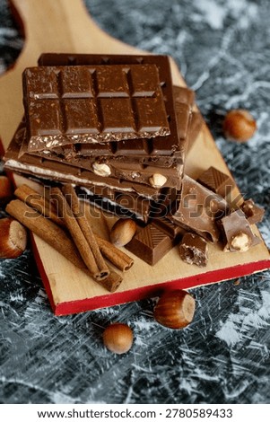 Stack of assorted chocolate bars with hazelnuts and cinnamon sticks on a wooden board