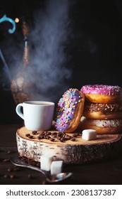 Stack of assorted donuts and a cup of steaming coffee on a dark background.