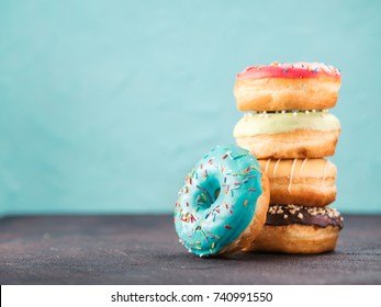 Stack of assorted donuts on black and blue cement background. Blue glazed doughnut with sprinkles on foreground. Copy space. Shallow DOF