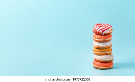 Stack Of Assorted Donuts On Blue Background. Many Colorful Glazed Doughnut With Sprinkles Stacked With Copy Space. Long Horizontal Banner